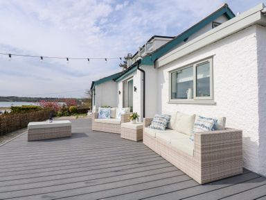 An outdoor deck with wicker sofas and a coffee table next to a white building at Swn Y Wylan Red Wharf Bay near Benllech