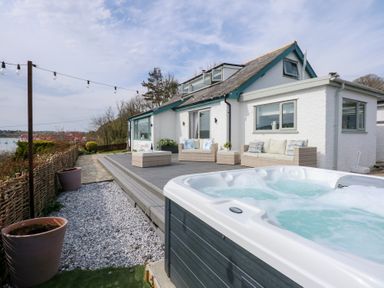 An outdoor patio with a hot tub seating area and a white house at Swn Y Wylan Red Wharf Bay near Benllech