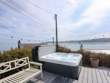 An outdoor deck with a hot tub bench string lights and sea view at Swn Y Wylan in Red Wharf Bay near Benllech