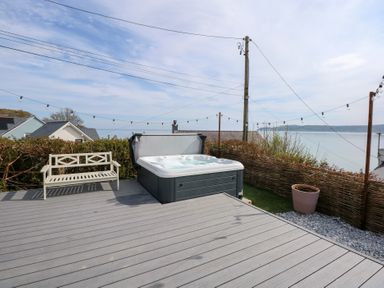 A deck with a hot tub a bench string lights and a view of the sea at Swn Y Wylan Red Wharf Bay near Benllech
