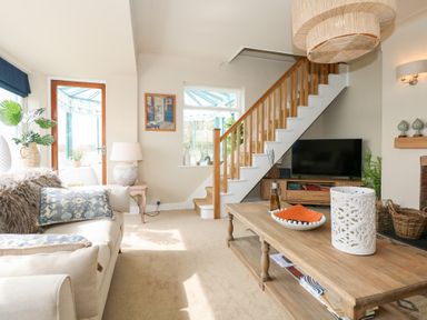 A living room with a sofa a wooden coffee table a television under stairs and a door leading to a conservatory at Swn Y Wylan Red Wharf Bay near Benllech