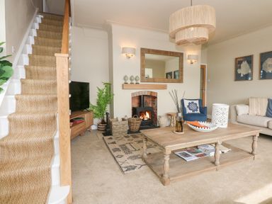 A living room with a staircase carpeted in wicker a wooden coffee table and a fireplace at Swn Y Wylan Red Wharf Bay near Benllech