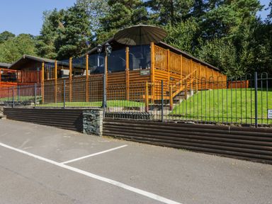A wooden cabin with a fenced deck and umbrella surrounded by trees at Lakeland View Ambleside 86 White Cross Bay near Windermere