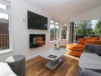 A living room with a wall-mounted tv and fireplace orange and gray seating and a coffee table at Lakeland View Ambleside 86 White Cross Bay near Windermere