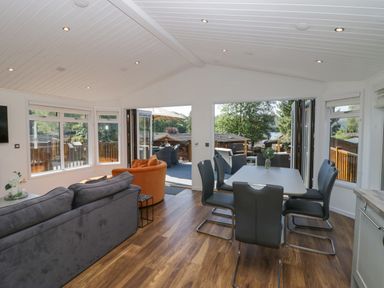 A dining area with a white table and six black chairs next to a living area with sofas and large windows at Lakeland View Ambleside 86 White Cross Bay near Windermere