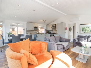 A living area with orange and gray sofas a coffee table a dining table with chairs and a kitchen at Lakeland View Ambleside 86 White Cross Bay near Windermere