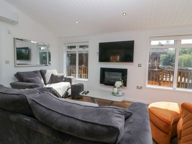 A living room with grey sofas a wall mounted TV and a fireplace at Lakeland View Ambleside 86 White Cross Bay near Windermere