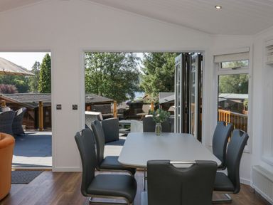 A dining area with a table and six chairs and an open door leading to an outdoor seating area at Lakeland View Ambleside 86 White Cross Bay near Windermere
