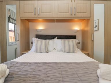 A bedroom with a bed with pillows and a blanket built-in wooden cabinets with mirrors on the doors and wall lights at Lakeland View Ambleside 86 White Cross Bay near Windermere