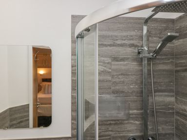A bathroom with a glass shower enclosure, rainfall and handheld showerheads, and a wall mirror reflecting a bedroom at Lakeland View Ambleside 86 White Cross Bay near Windermere