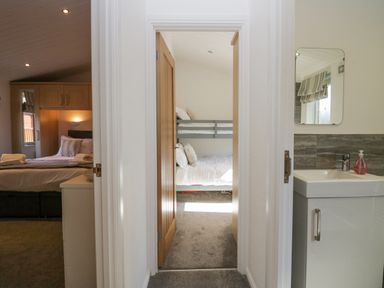 A hallway showing a bedroom with bunk beds in the center and a bedroom with a double bed to the left and a bathroom sink with mirror to the right at Lakeland View Ambleside 86 White Cross Bay near Windermere