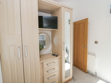 A wardrobe unit with a television remote a round mirror and a vase of foliage next to a wooden door in a bedroom at Lakeland View Ambleside 86 White Cross Bay near Windermere