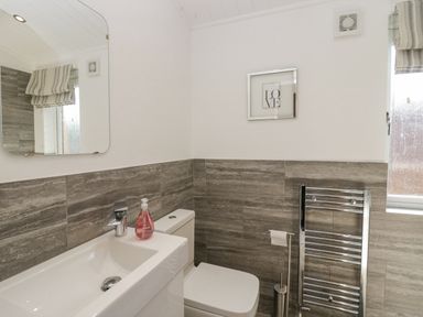 A bathroom with a sink and faucet a toilet a wall mirror towel rack and a framed love artwork at Lakeland View Ambleside 86 White Cross Bay near Windermere