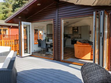 A deck with outdoor seating and open doors leading to a dining area and kitchen at Lakeland View Ambleside 86 White Cross Bay near Windermere