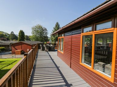 A wooden deck with outdoor dining furniture attached to a building with large windows at Lakeland View Ambleside 86 White Cross Bay near Windermere