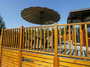 An outdoor wooden deck with a large umbrella and wicker chairs at Lakeland View Ambleside 86 White Cross Bay near Windermere