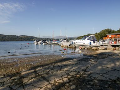 A lakeside boat dock with boats moored and birds near the shore at Lakeland View Ambleside 86 White Cross Bay near Windermere