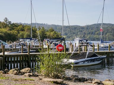 A marina with several boats docked by wooden piers near trees and hills at Lakeland View in Ambleside 86 White Cross Bay near Windermere