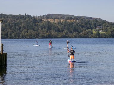 Four people paddleboarding on a lake with forested hills in the background at Lakeland View Ambleside 86 White Cross Bay near Windermere