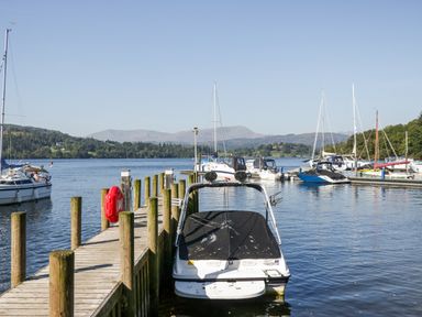 A dock with boats moored on a lake with hills in the background at Lakeland View Ambleside 86 White Cross Bay near Windermere