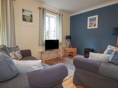 A living room with two grey sofas a wooden table with a television a window with striped curtains and blue and cream walls at Coombe Cottage in Falmouth
