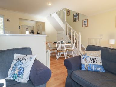 A living area with two armchairs and decorative pillows and a round dining table with chairs near stairs at Coombe Cottage in Falmouth