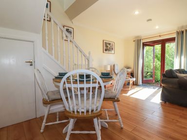 A dining area with a round table and four chairs next to stairs and a living space with sofa and open glass door at Coombe Cottage in Falmouth