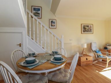 A dining area with a round table set for four near a staircase and a seating area with a chair and lamp at Coombe Cottage in Falmouth