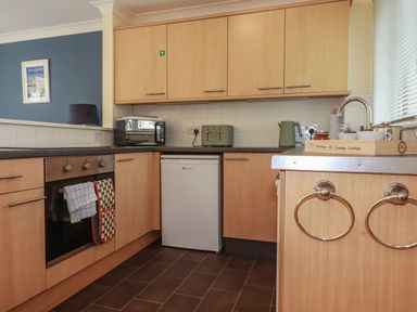 A kitchen with wooden cabinets a toaster kettle oven and a small refrigerator at Coombe Cottage in Falmouth