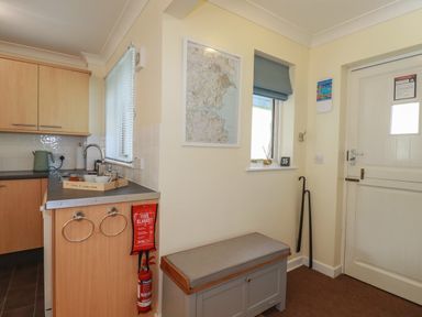A kitchen counter with a sink and kettle next to a bench and a door with a window at Coombe Cottage in Falmouth