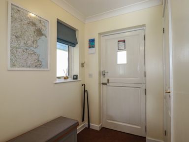 A small entrance hallway with a white door a window with a blue blind a map on the wall a bench and walking sticks at Coombe Cottage in Falmouth