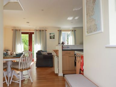 A dining area with a round table and chairs next to a living room with a sofa and windows with curtains at Coombe Cottage in Falmouth