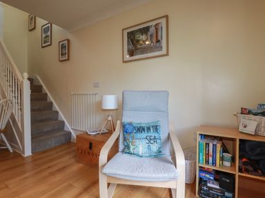 A stairway with framed pictures a chair with a swim in the sea pillow a wooden side table with a lamp and bookshelf with books and a basket at Coombe Cottage in Falmouth