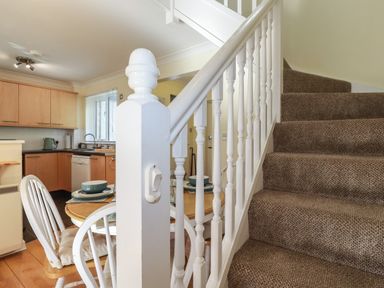 A carpeted staircase with white wooden banister next to a small dining table and chairs near a kitchen at Coombe Cottage in Falmouth