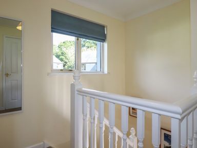 A stairway with white railing and a window with a blue blind at Coombe Cottage in Falmouth