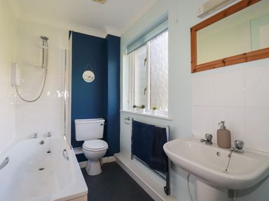 A bathroom with a bathtub, toilet, sink, mirror, and window at Coombe Cottage in Falmouth