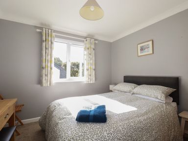 A bedroom with a bed and folded towels on it next to a window with curtains at Coombe Cottage in Falmouth