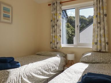 A bedroom with two single beds a small bedside table with a lamp and a window with patterned curtains at Coombe Cottage in Falmouth