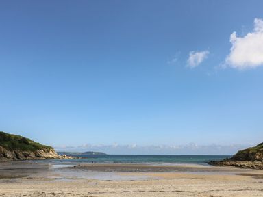 A sandy beach with shallow water between two rocky cliffs under a clear blue sky at Coombe Cottage in Falmouth