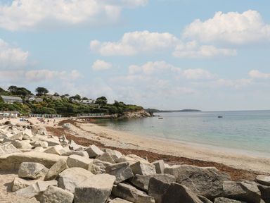 A beach with rocks in the foreground people on the sand colorful beach huts on the hillside and houses at Coombe Cottage in Falmouth