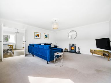 A living room with a blue sofa a fireplace a round mirror and a television at Fairwinds in Portreath