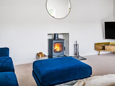 A living room with a wood burning stove fire and blue sofas at Fairwinds in Portreath