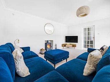A living room with blue sofas a wood burning stove and a television at Fairwinds in Portreath