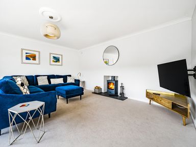 A living room with a blue sectional sofa a fireplace a wall-mounted TV and a wooden TV stand at Fairwinds in Portreath