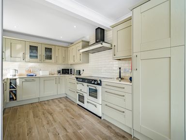 A kitchen with beige cabinets a stove microwave and wooden floor at Fairwinds in Portreath