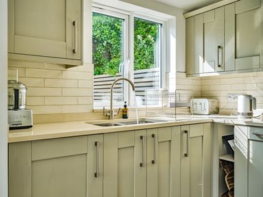 A kitchen with a sink running water a window above it a toaster a kettle and cabinets at Fairwinds in Portreath