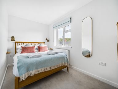A bedroom with a wooden bed frame blue blanket and two pink pillows at Fairwinds in Portreath