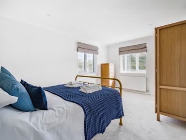 A bedroom with a metal bed frame blue bedding wooden wardrobe and dresser under windows at Fairwinds in Portreath