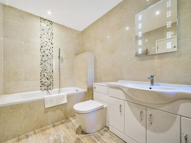 A bathroom with a bathtub shower combination toilet and white vanity with illuminated mirror at Fairwinds in Portreath