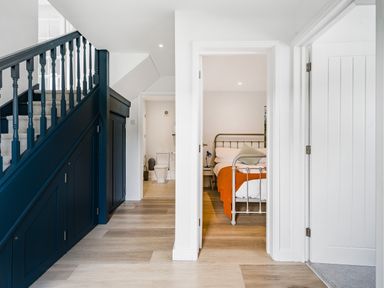 A hallway with blue staircase paneling and multiple doors leading to a bedroom and a bathroom at Fairwinds in Portreath